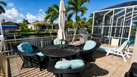 Round wicker dining set with umbrella on canal terrace beside gas grill and pool screen