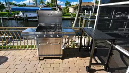 Stainless steel gas barbecue with side burner and prep table facing canal and boat docks