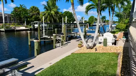 Boat dock with lift, swim ladder, palm trees and stacked white Adirondack chairs by canal