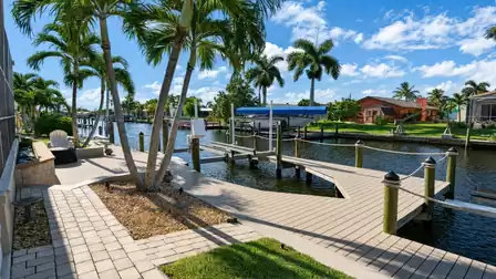 Wide boat dock with rope railings, boat lift and paved path under multiple palm trees