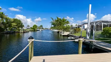 Canal from wooden dock with rope railing, screened patios and boat lift right