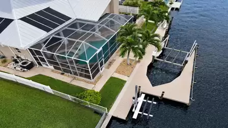 Aerial view of screened pool patio, palm trees and dock with boat and jet ski lifts