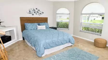 Bedroom with queen-size bed, three arched windows, blue rug and wicker pouf