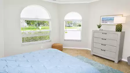 Bedroom corner with two arched windows, dresser with lamp, wicker stool and bed