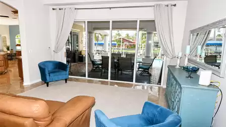 Living room seating with leather sofa, two blue chairs and view to pool patio