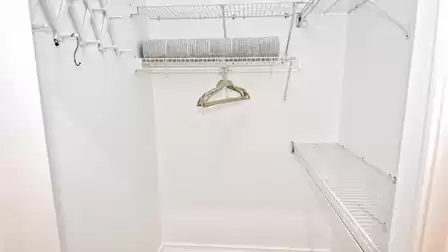 Walk-in closet with wire shelving, hanging rail, hangers and rolled blanket on shelf