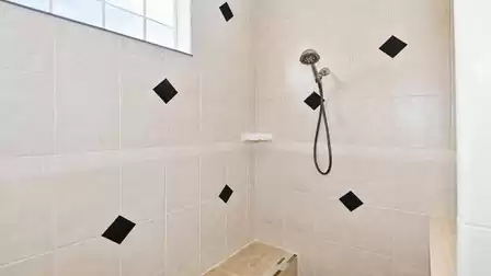 Walk-in shower with beige tiles, built-in bench, handheld shower and corner soap shelf