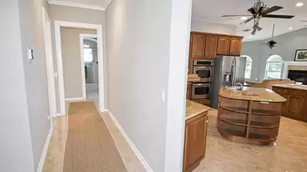 Hallway with runner rug leading to kitchen with island, double oven and living area