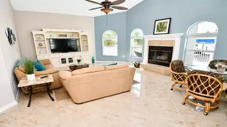 Living area with Smart TV wall unit, tan sofas, fireplace and round rattan table