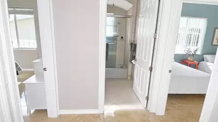 Hallway with open doors to bathroom with glass shower and two tiled bedrooms