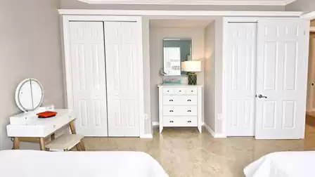 Bedroom wall with white vanity table, dresser between two closets and tiled floor