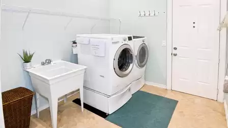 Laundry room with front-load washer, dryer, utility sink, wicker basket and door on blue mat