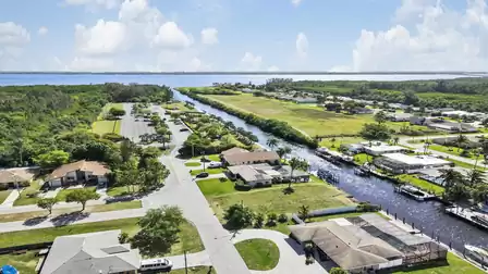 Aerial view of residential canal with docks, parking lot, houses and open green strip