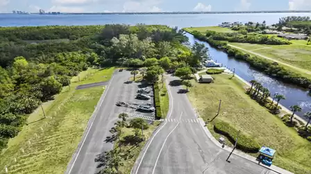 Parking area beside canal and marina, bordered by dense trees and distant bay