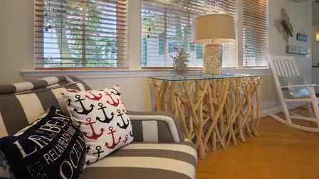 Striped armchair with anchor cushions beside driftwood console table and white rocking chair