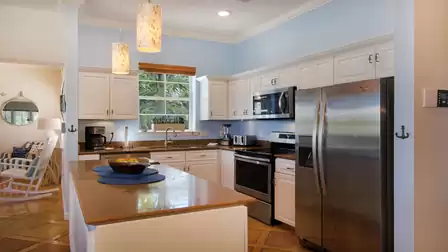 Kitchen with island, stainless steel fridge, window to palm trees and rocking chair