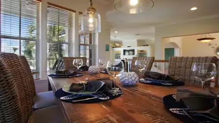 Dining table with wicker chairs, set with glassware and navy placemats by windows