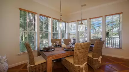 Corner dining area with wicker chairs, wooden table and large windows to pool