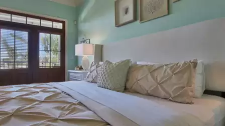 Bedroom with tufted bedding, wall art and glass doors with blinds to palms