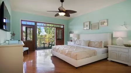 Bedroom with upholstered bed, balcony doors to palm trees and ceiling fan