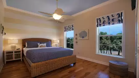 Bedroom with wicker bed, striped bedding, ceiling fan and two windows to canal