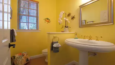 Yellow bathroom with pedestal sink, gold fixtures, window and crab wall decor