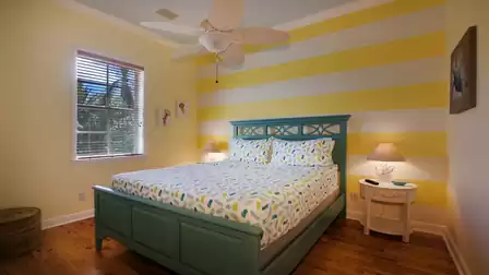 Bedroom with teal bed, yellow striped accent wall, ceiling fan and window