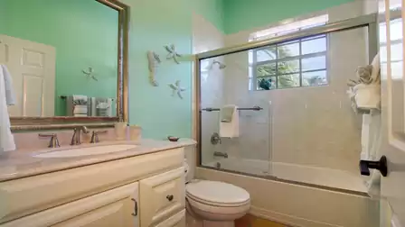 Green bathroom with tub shower, glass doors, seahorse wall decor and vanity