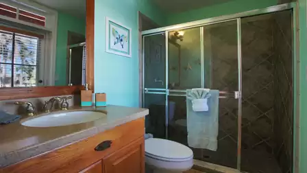 Bathroom with glass shower, green walls, wooden vanity and window with blinds