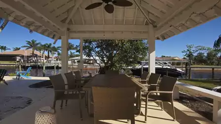 Canalside gazebo with wicker dining table, chairs and ceiling fan facing docked boat