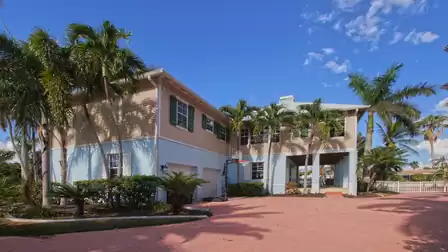 Two story house with palm trees, pink driveway and covered carport entrance