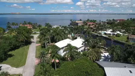 Aerial view of canalfront homes with white roofs, palm trees and wide river