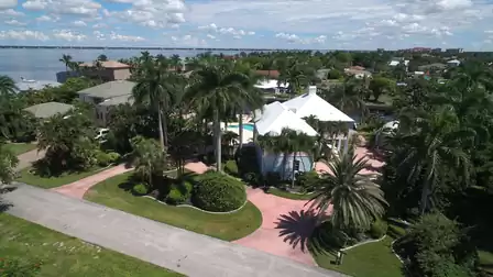 Aerial view of white house with pink circular driveway, palm trees and nearby river