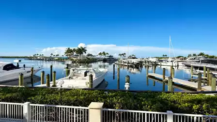 Marina with multiple motorboats at docks behind white fence and green hedge
