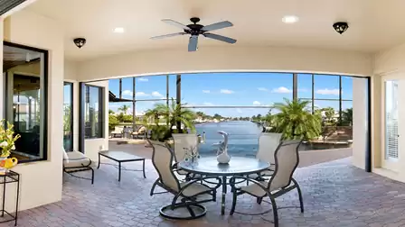 Covered pool patio with dining table, seating area, ceiling fan and canal view framed by palm trees