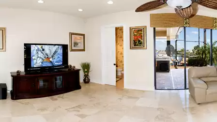 Living room with Smart TV, leather armchair, natural stone flooring and sliding door to the covered pool patio
