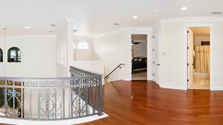 Upper-level gallery with hardwood flooring, decorative railing, staircase and access to bedroom and bathroom