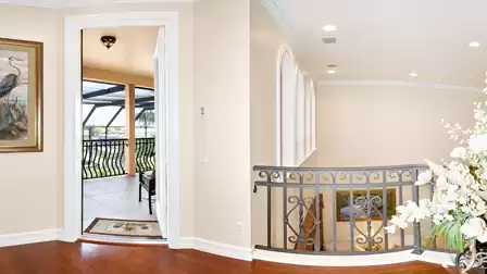 Upper-level gallery with hardwood flooring, decorative railing, arched windows and access to the covered balcony