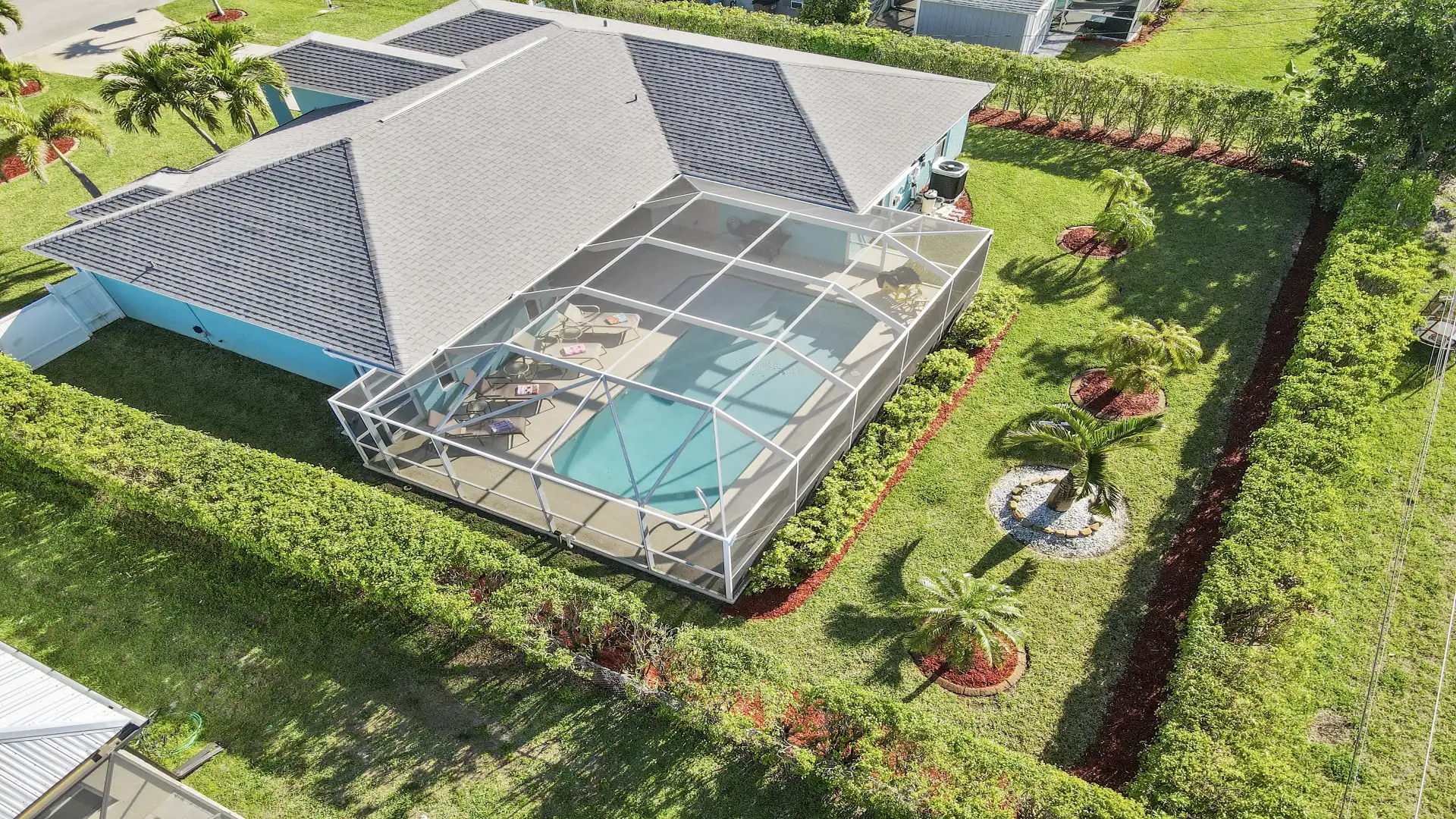 Fenced garden with palm trees and screened pool area.