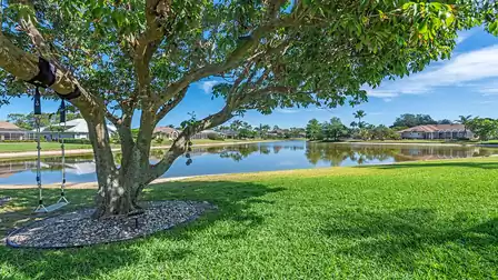 Green garden area with shady tree, lake swing and peaceful water view, surrounded by well-kept homes.