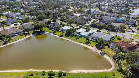 Aerial view of a lake surrounded by villas, palm trees and well-kept gardens in a quiet residential area.